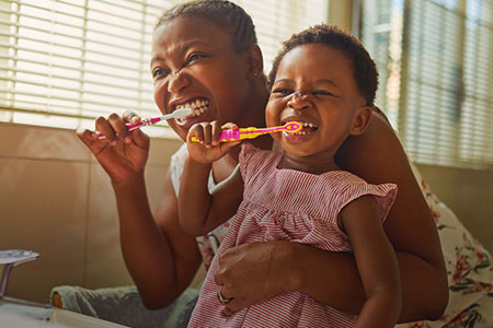 Imagem de uma criança escovando os dentes com uma mulher adulta